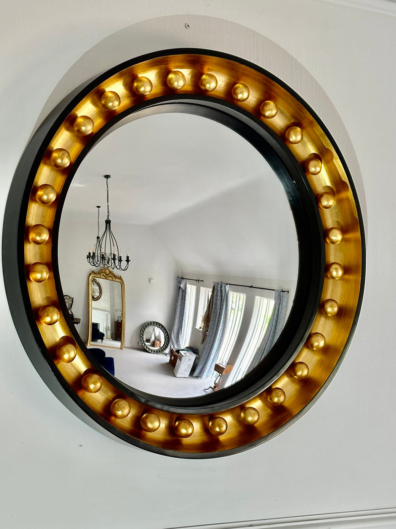 Round mirror with gold embellishments on a white wall