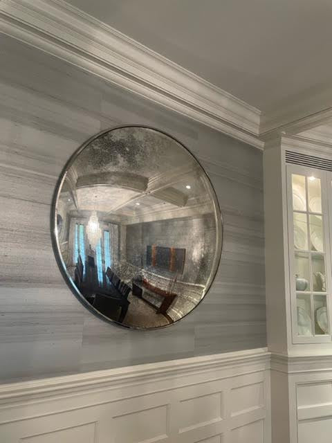 Antiqued silver convex wall mirror with a polished silver frame, displayed in an interior setting.